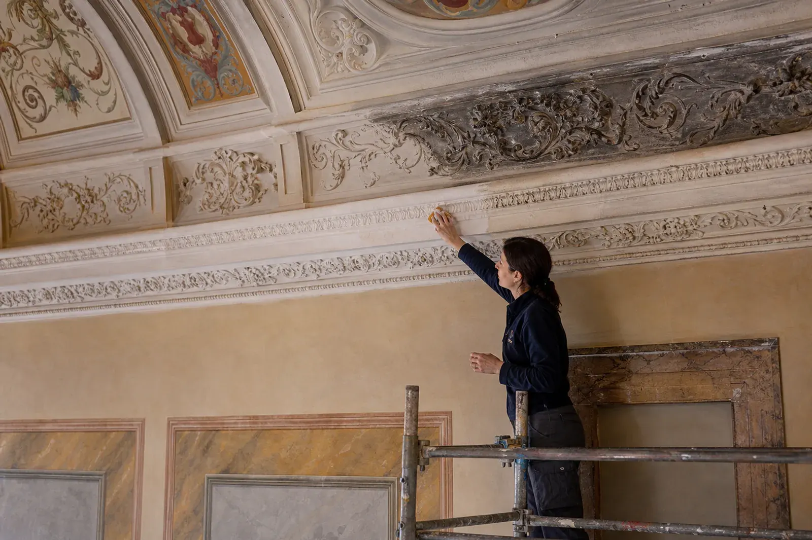 Restauratrice al lavoro su una cornice decorata, dal ponteggio